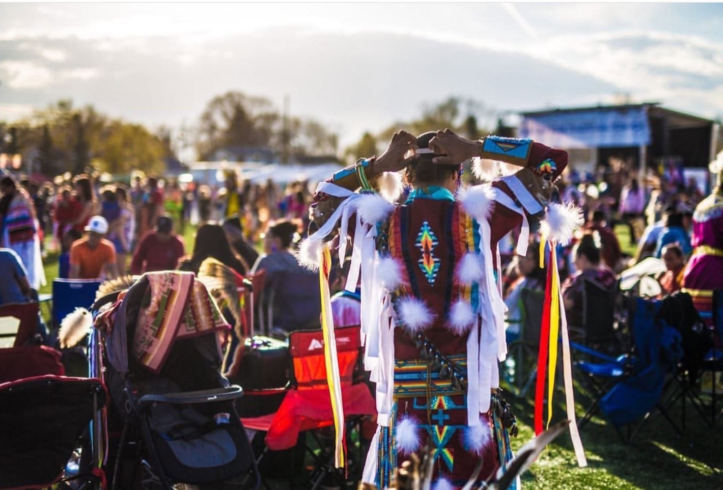 A dancer in beaded regalia, seen from behind, looking out over the powwow crowd